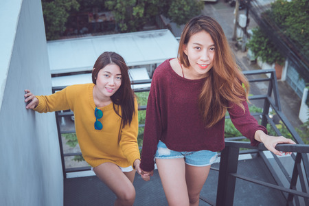 Lovely lesbian couple together concept. Couple of young asian women walking up the stairs to top roof.の写真素材