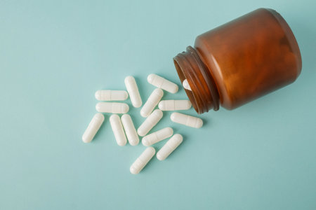 Top view bottle container with medication capsules on blue background with copy space. Beauty,...