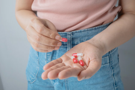 Close up woman hand holding red and white tablet pill on hand. Beauty, wellness, healthcare and medicine concept.の写真素材