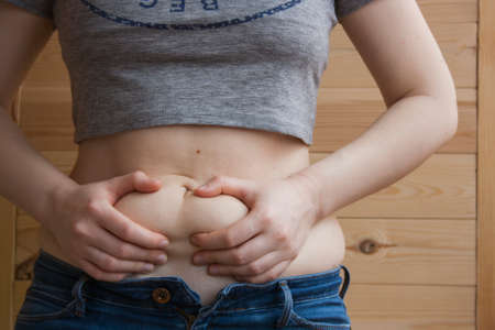 Overweight woman, hand holding excessive belly fat. Concept to reduce belly and shape up healthy stomach muscleの写真素材