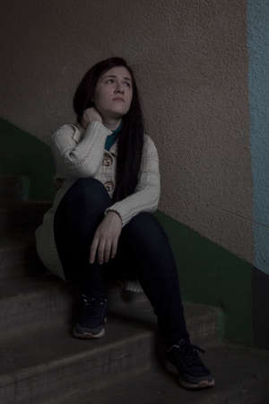 Sad girl sitting on the stairs at the entrance of the houseの写真素材