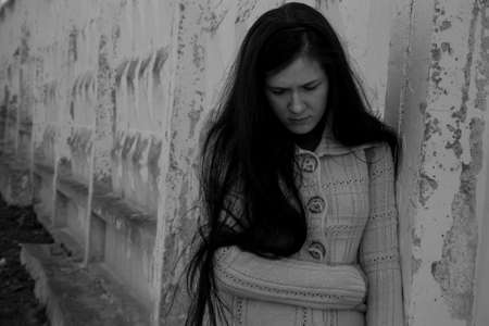 A crying young girl in depression stands leaning against an old wall.の写真素材