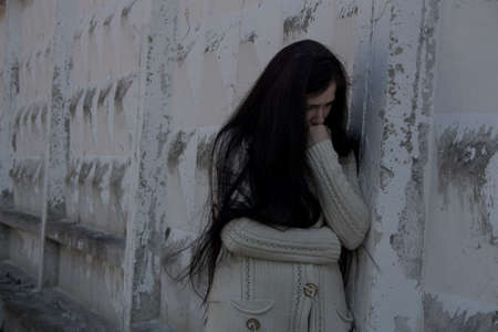 A crying young girl with depression stands leaning against an old brick wall.の写真素材