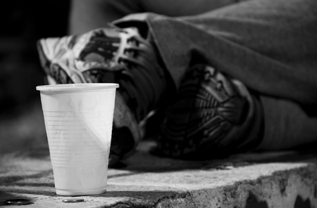 Homeless lying on bench next to cup and coinsの写真素材