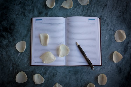 Romantic image of notebook and pen with rose petalsの写真素材
