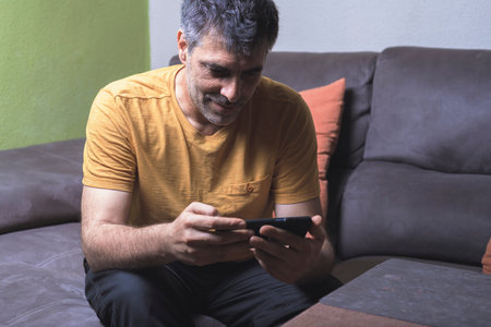 Relaxed moment. A man enjoying the comfort of the sofa while using his mobile phone. Conveys comfort and technology in harmony.の写真素材