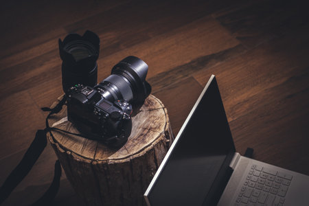 Camera with lens on tree trunk and laptop in dark and rustic environment.の写真素材