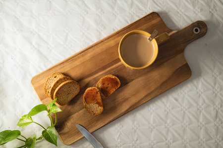 Light breakfast of toast with jam and a large orange cup of coffee on a wooden board in white...