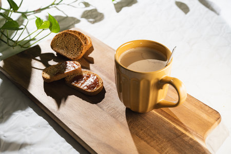 Light breakfast of toast with jam and a large orange cup of coffee with milk on a wooden board in white background.の写真素材