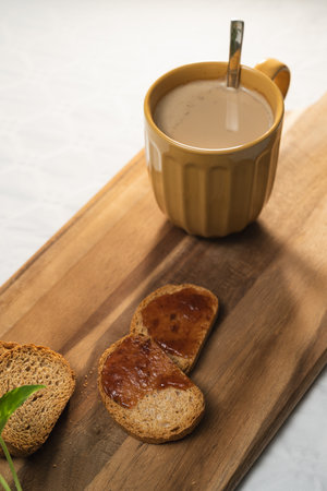 Light breakfast of toast with jam and a large orange cup of coffee with milk on a wooden board in...