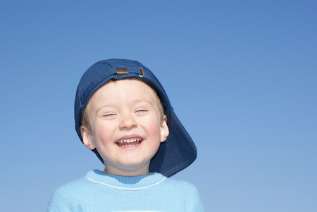 Happy boy laughs, in a baseball cap, background skyの写真素材