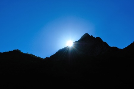 Bright sun at sunset, hiding behind the mountain, sparkling raysの写真素材