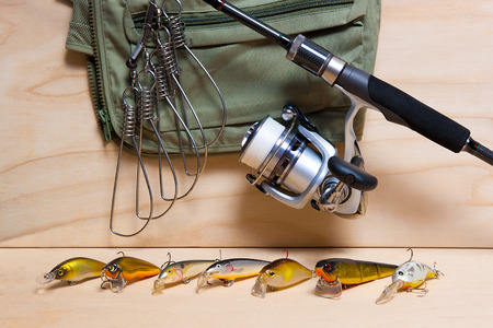 Fishing rod, reed, plastic baits on wooden table. Fish stringer on the backgroud.
