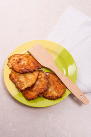 Homemade potato pancakes. Potato fritters with meat on green plate and wooden spoon on light background. Traditional Belarusian and Ukrainian cuisine.の写真素材
