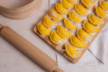 Several ready for boiling vareniki, dumplings, pierogi with cottage cheese or curd on wooden cutting board with flour. Wooden rolling pin, sieve on light marble background. 
の写真素材