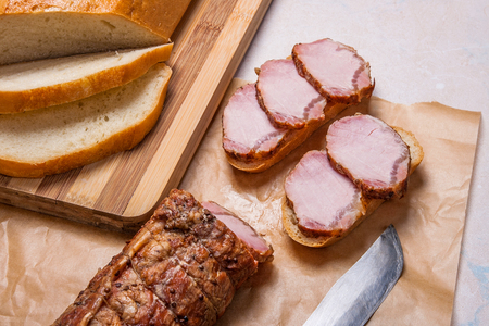 Slices smoked with spice and herbs meat or ham on brown packing paper. Slices white wheat bread on wooden cutting board. Small snacks of bread and meat and old vintage knife. Brown cloth on back background. Composition on light marble background.
の写真素材