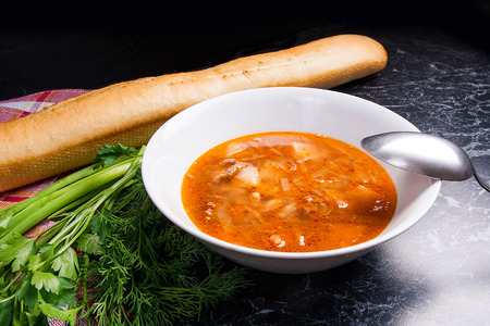 Vegetables and meat in red beetroot soup or borsch in white plate. White bread, herbs - dill, green onion, parsley around the plate with metal spoon. Ukrainian tomato soup borsch on dark marble background.
の写真素材