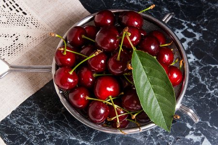 Ripe sweet cherries with big green leaf of cherry tree  in steel colander. Composition in rustic...