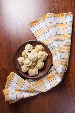 Boiled homemade meat dumplings served in clay plate with creamy sauce. Composition in rustic style on wooden background with boiled Ukrainian ravioli.の写真素材