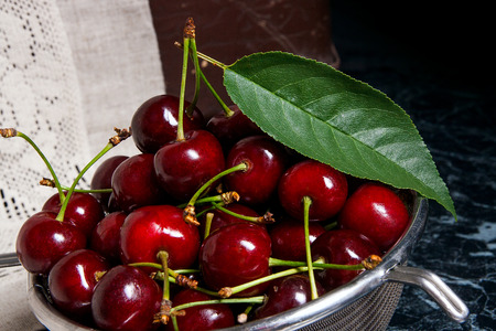 Ripe sweet cherries in steel colander on marble table. Composition in rustic style - organic red...