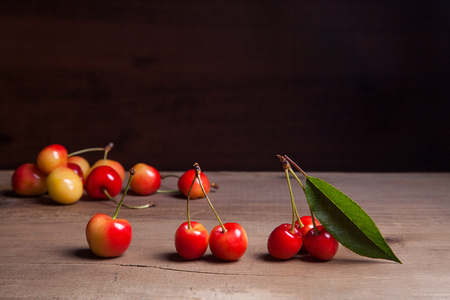 Berries of yellow sweet cherries with green leaf of cherry tree on vintage wooden backgroundの写真素材