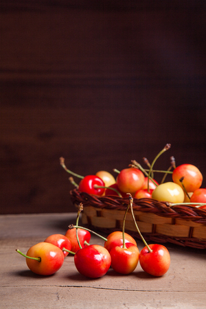 Berries of yellow sweet cherries in yellow wooden basket and several fruit on vintage wooden backgroundの写真素材