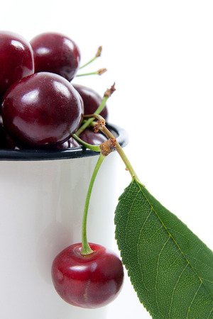 White cup with ripe berries of red sweet cherry and several berries in front of the cup. Composition on a white background.の写真素材