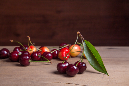 Berries of red and yellow sweet cherries with green leaf of cherry tree on vintage wooden backgroundの写真素材