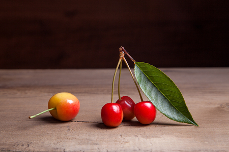 Berries of yellow sweet cherries with green leaf of cherry tree on vintage wooden backgroundの写真素材