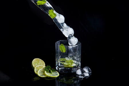 Mojito summer beach refreshing tropical cocktail in glass with splash soda water, lime juice, mint leaves, sugar, ice and rum on reflective black surface.の写真素材