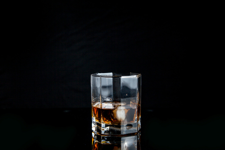 Drinks and beverages conception. Single glass of whisky with ice cubes on reflective black surface.の写真素材