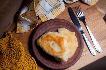 Clay plate with two of individual fried pies with meat on wooden table. Composition of fast food dinner and cutlery in rustic style on vintage wooden background.の写真素材