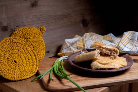 Clay plate with two of individual fried pies with meat on wooden table. Composition of fast food dinner - plate with two pies with pulled pork pastry, cutlery and green onian on vintage wooden background. の写真素材