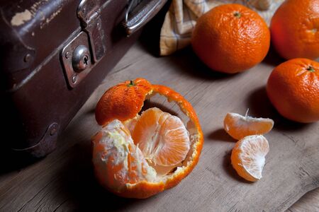 Several of unpeeled whole fresh orange mandarine or oranges, tangerines, clementines, citrus fruits, one fruit is half peeled and slices of peeled mandarin on wooden board
の写真素材