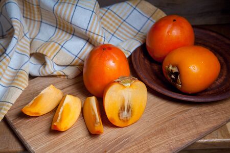 Composition of ripe delicious whole persimmon fruits, half and sliced fruit ready for eat on wooden background.の写真素材