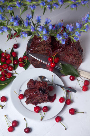 Composition on white background - delicious chocolate cake with sweet cherry, white plate with part...
