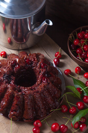 Composition on dark wooden background - delicious chocolate cake with sweet cherry, vintage kettle, clay bowl with berry of sweet cherry and leaves of cherry tree.の写真素材