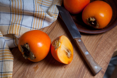 Composition of ripe delicious whole persimmon fruits, half and sliced fruit ready for eat with vintage knife on wooden background.の写真素材