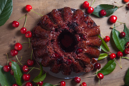 Composition on dark wooden background - delicious chocolate cake with sweet cherry, clay bowl with berry of sweet cherry and leaves of cherry tree.の写真素材