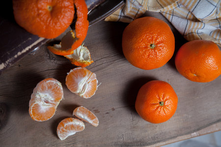Several of unpeeled whole fresh orange mandarine or oranges, tangerines, clementines, citrus fruits, one fruit is half peeled and slices of peeled mandarin on wooden boardの写真素材