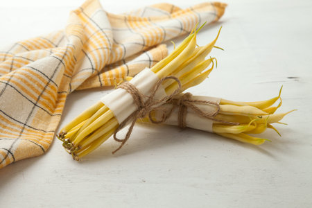 Two bunches of raw yellow pods of haricot and yellow kitchen towel on wooden white background....