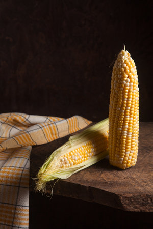 Two ears of ripe sweet corn on wooden background. Cobs with white and yellow grains. Fresh ear of...
