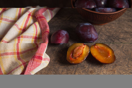 Juicy summer plum fruit. Several whole and half of ripe sweet plums on vintage wooden background. Clay plate with plums on background.の写真素材