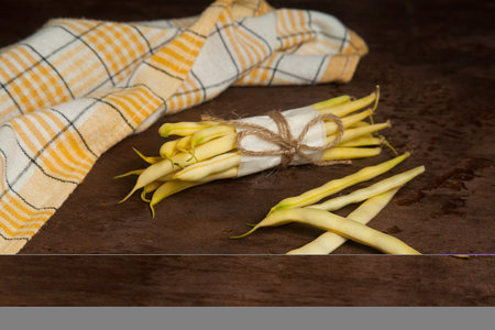 Bunch and several pods of raw yellow pods of haricot with yellow kitchen towel on wooden background. French beans or Green beans also known as String beans from India. Vegetables collection.の写真素材