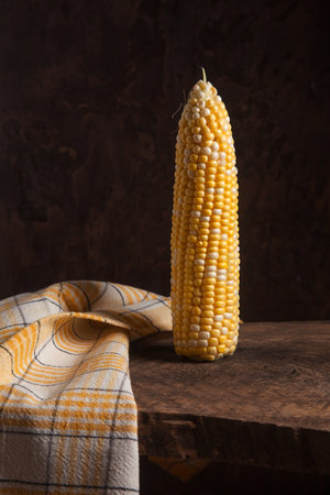 One ear of ripe sweet corn on wooden background.