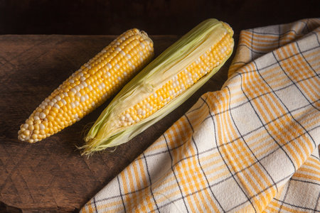 Two ears of ripe sweet corn on wooden background. Cobs with white and yellow grains. Fresh ear of...