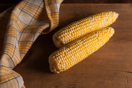Two ears of ripe sweet corn and yellow towel on vintage wooden background. Cobs with white and yellow grains.の写真素材
