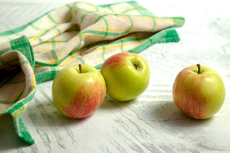 Three fresh green apples on white wooden background with green kitchen towel.の写真素材