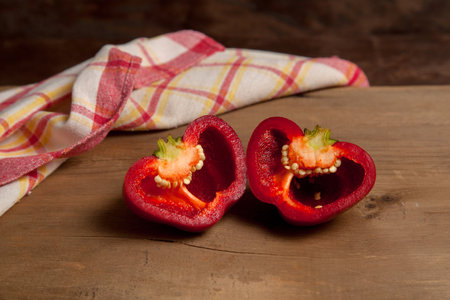 Halves of red bell pepper (capsicum) known as sweet bell pepper, paprika on vintage wooden background with red kitchen towel.の写真素材