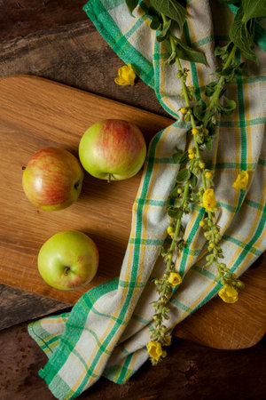 Cutting board with three fresh green apples on wooden background with green kitchen towel.の写真素材